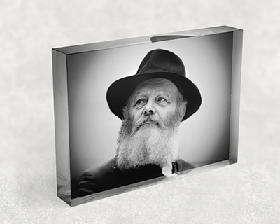 תמונה בשחור לבן של הרבי מליובאוויטש מביט הצידה על בלוק אקרילי